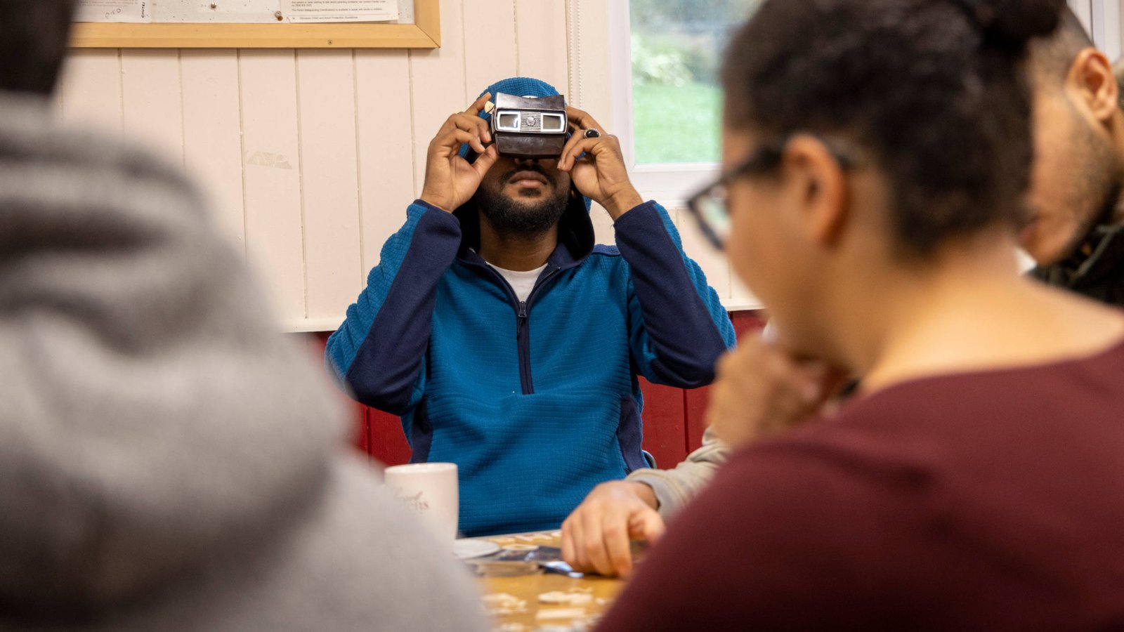 A young male refugee looks into a stereoscope which obscures his upper face